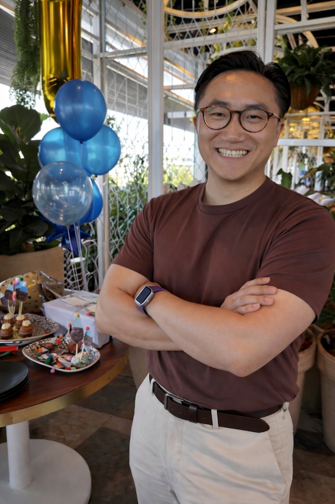 Jason Lu smiling with his arms folded in a garden setting